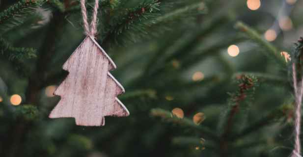 Holzanhänger in Weihnachtsbaum-Form hängt vor einem grünen Tannenhintergrund
