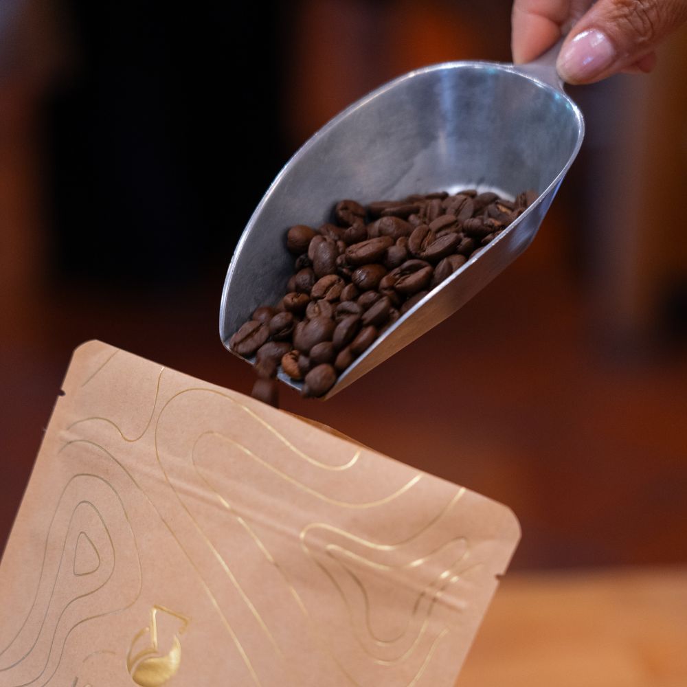 Kaffeebohnen werden mit einer Schaufel in eine Packung El Paraíso Lychee gefüllt