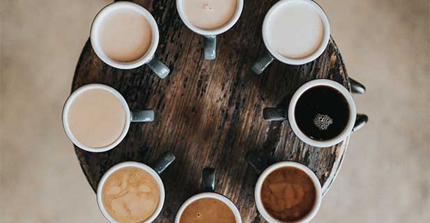 verschiedene Tassen mit Kaffee stehen im Kreis auf einem Holztablett