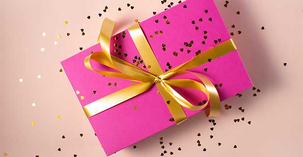 Kategoriebild Geschenke Geschenk in pink verpackt mit goldenem Geschenkband und goldenem Konfetti