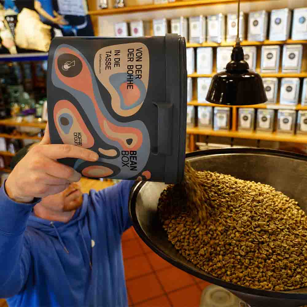 Mitarbeiter schüttet Rohkaffee aus unserem Mehrwegeimer in die Öffnung des Rösters