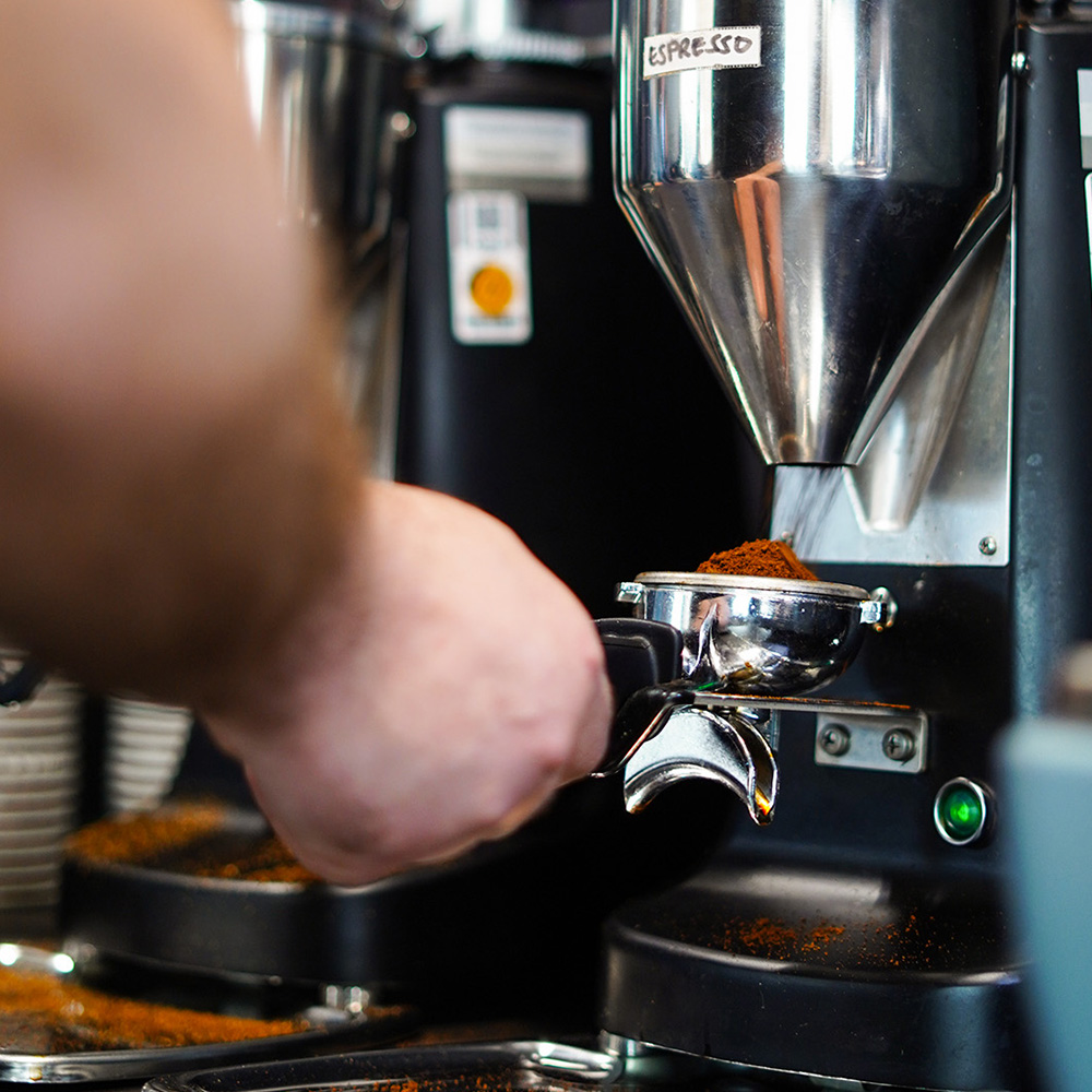 Siebträger unter einer Kaffeemühle mit hochwertigen Kaffeebohnen für die frische Espressozubereitung.