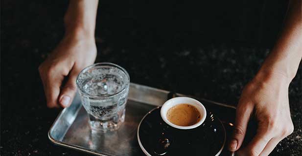 Kategoriebild Pads Ein Espresso und ein Glas Wasser werden auf einem Tablett serviert