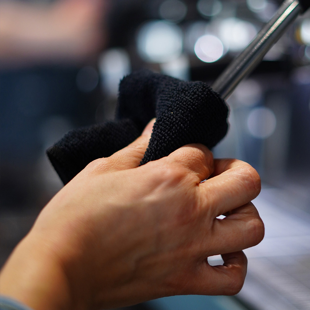Barista reinigt die Dampflanze einer Siebträgermaschine nach der Zubereitung eines Cappuccinos.