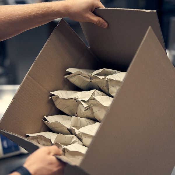 Acht beige Kaffeepäckchen in einem Karton verpackt, der von zwei Händen gehalten wird