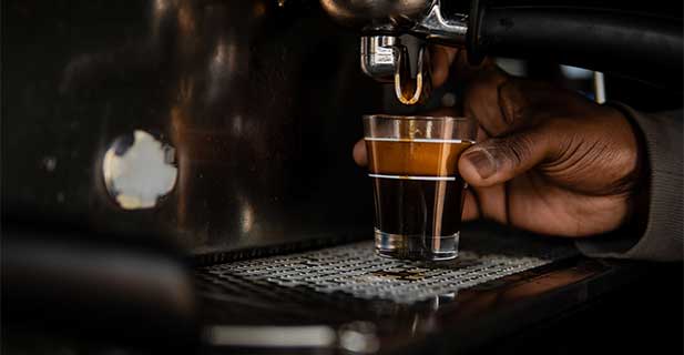 Kategoriebild Workshop Hand hält ein Espressoglas unter den Auslass eines Siebträgers, das Glas ist voll Espresso