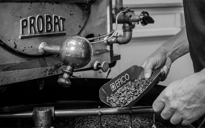 Röster Probat schwarz-weiß Bild: Auschnitt eines Probat Rösters. Im Vordergrund hält ein Mann eine Schale in der Hand, in der Kaffeebohnen sind