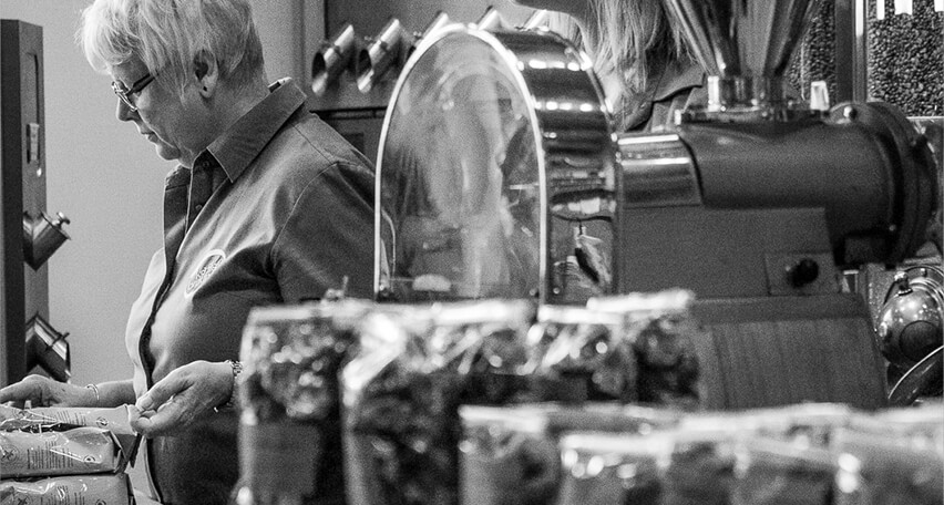 Röstereiverkauf Mitarbeiterin steht hinter Ladentheke und verkauft Kaffee, im Vordergrund stehen Päckchen mit Kaffeebonbons. schwarz-weißes Bild