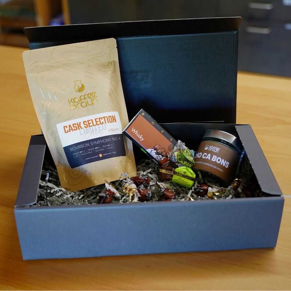 Geöffnete dunkelgraue Geschenkbox mit Cask Selection Bourbon Symphony No. 4, Zotter Whisky-Schokolade, Tartufo-Pralinen und Choca Bons