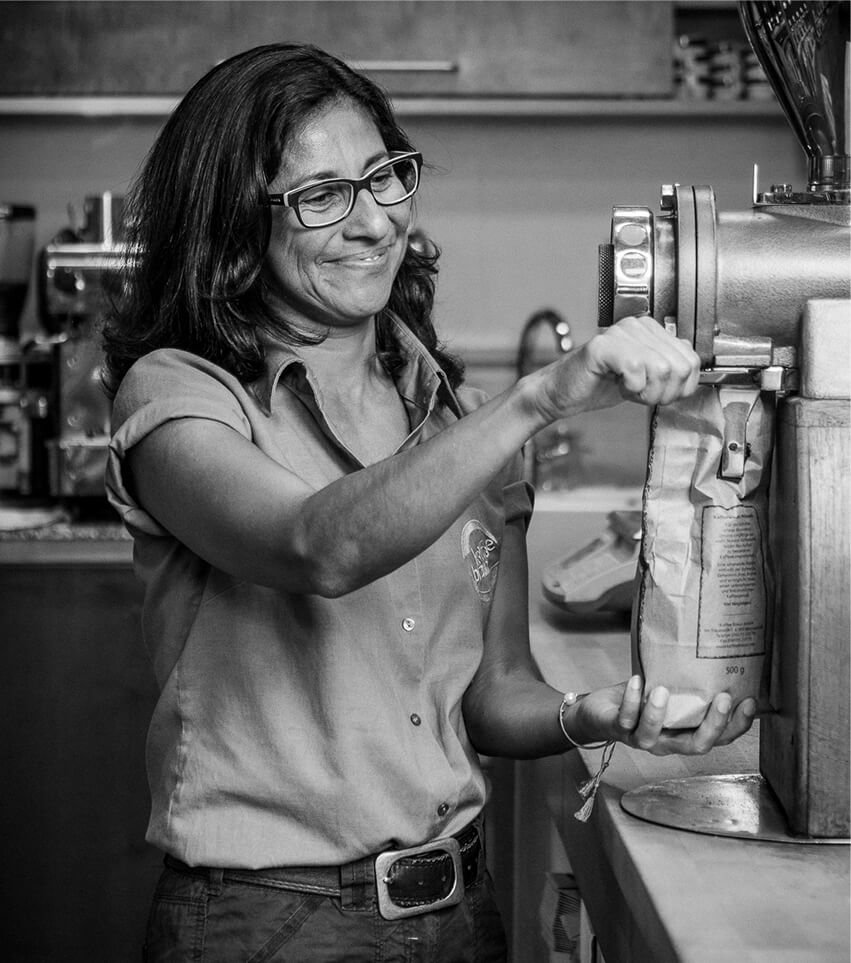 Röstereiverkauf Mühle schwarz-weiß Bild: Mitarbeiterhin steht lächelnd an der Kaffeemühle und mahlt den Kaffee in ein Päckchen