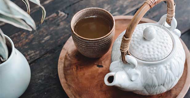Kategoriebild Tee weiße Teekanne und ein Porzellanbecher mit Tee auf einem braunen Holztablett