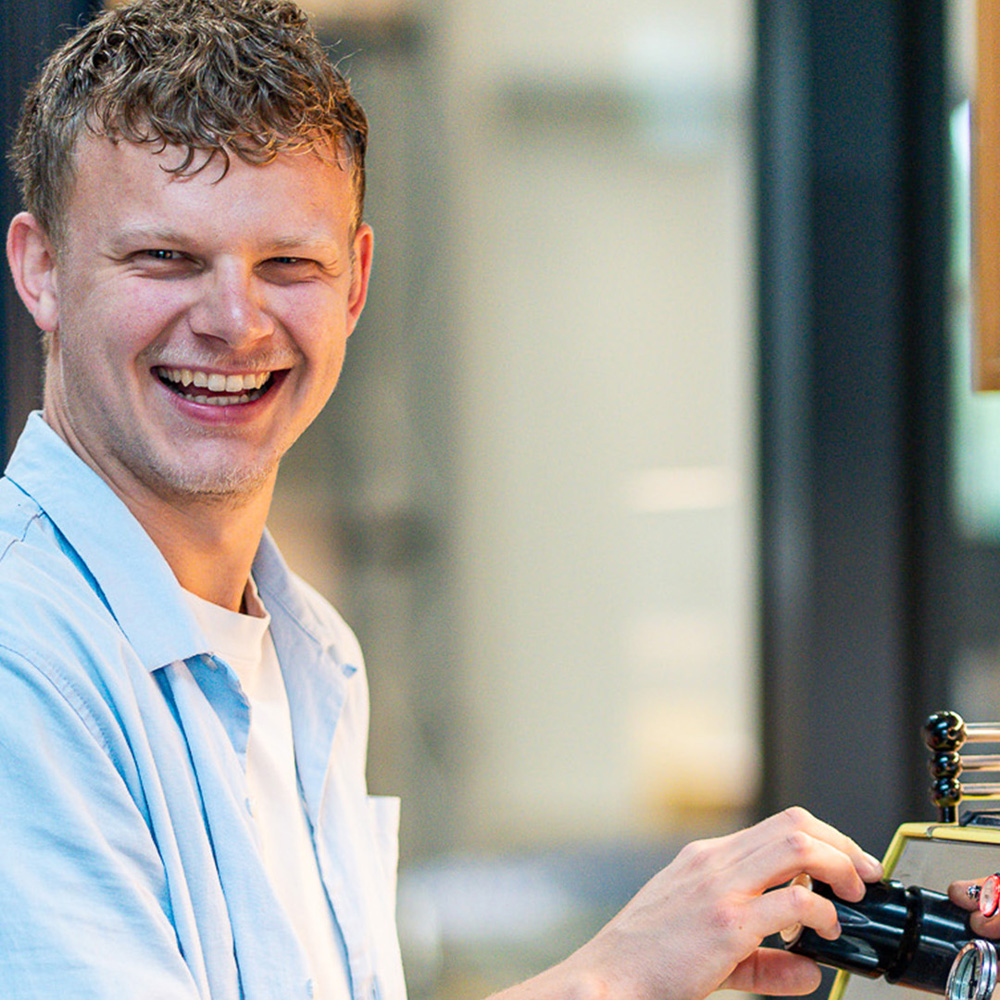 Mitarbeiter bedient eine professionelle Siebträgermaschine und bereitet frisch gerösteten Kaffee im Café- oder Office-Bereich zu.